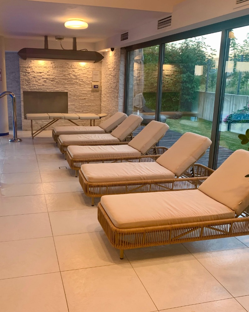 Leżaki przy basenie w strefie wellness, za oknem zieleń